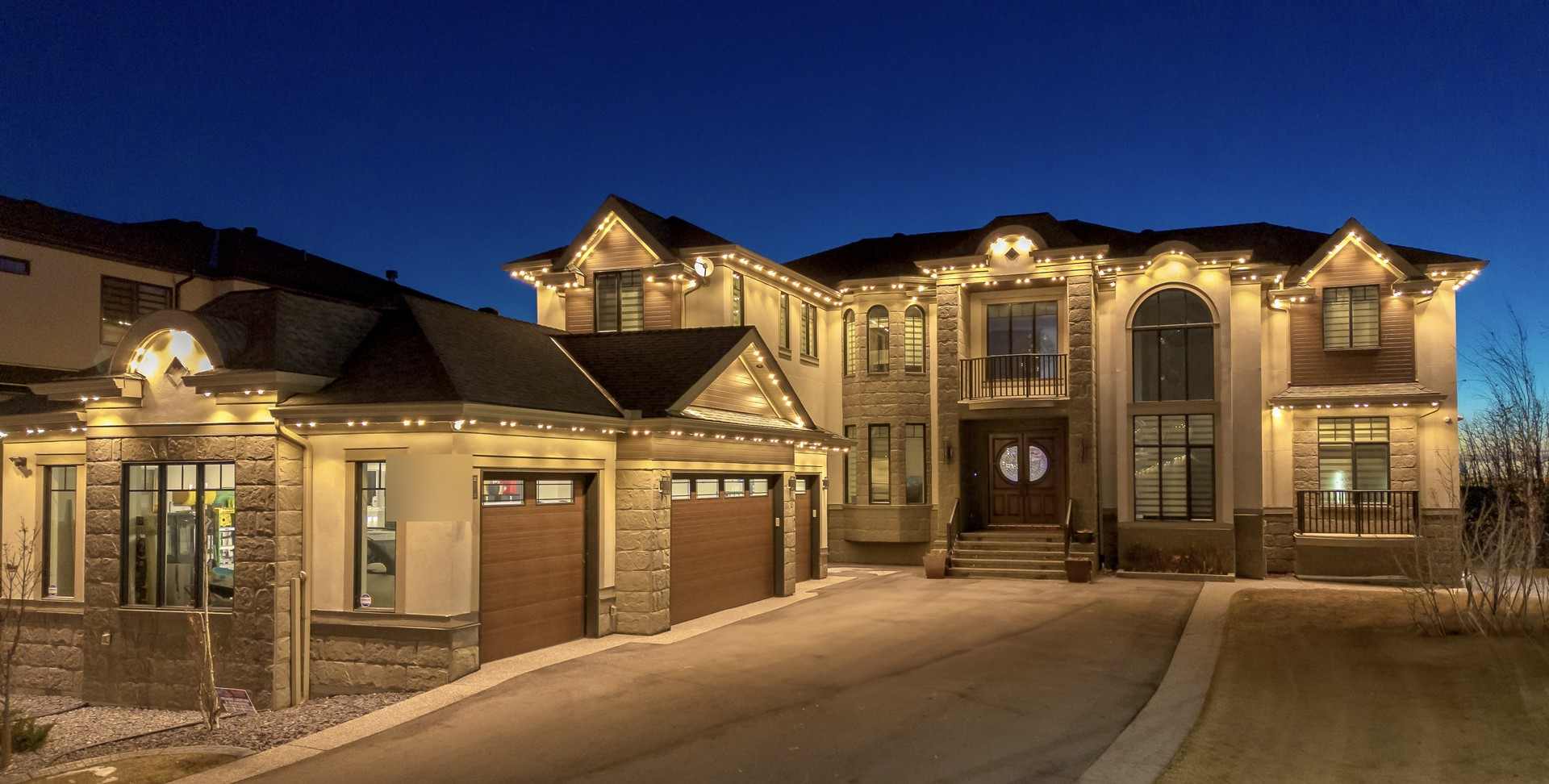A large stone-and-stucco home at blue hour, every gable, arch and eave outlined in warm white, with a lit portico over the front door.
