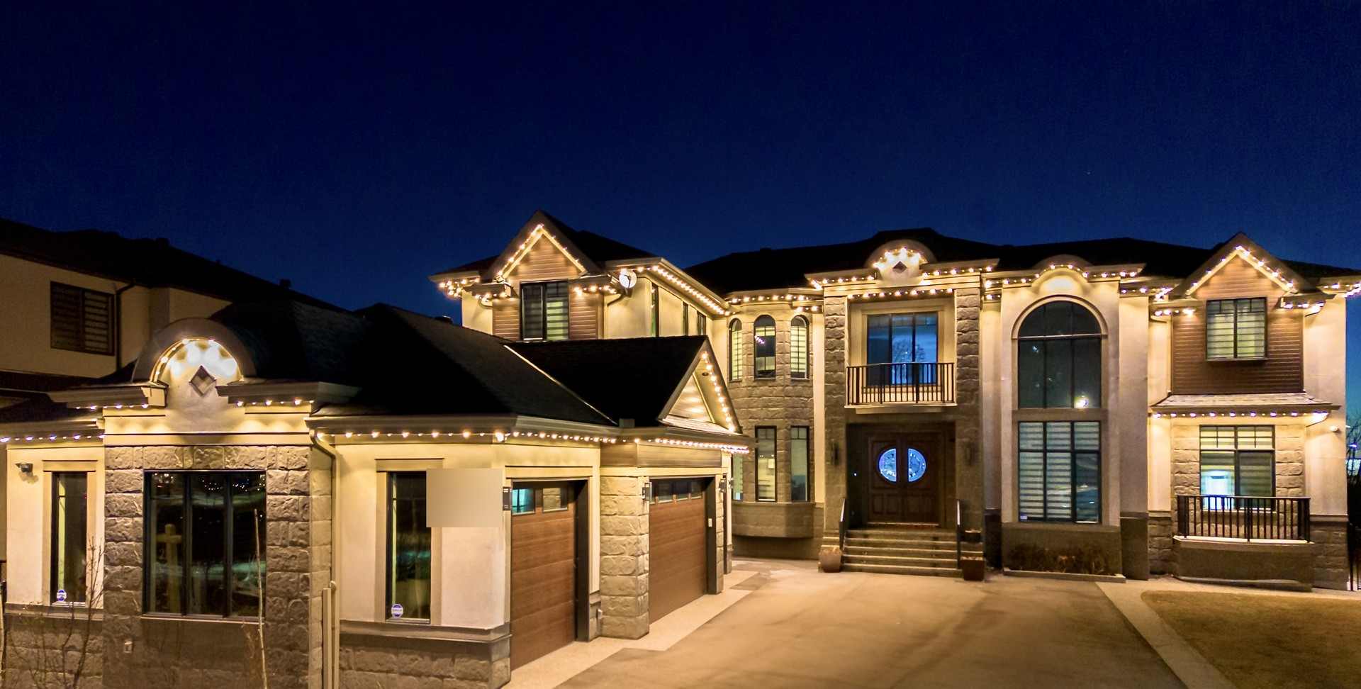 A stone-and-stucco home against a deep blue evening sky, a warm white run tracing three separate roof peaks.