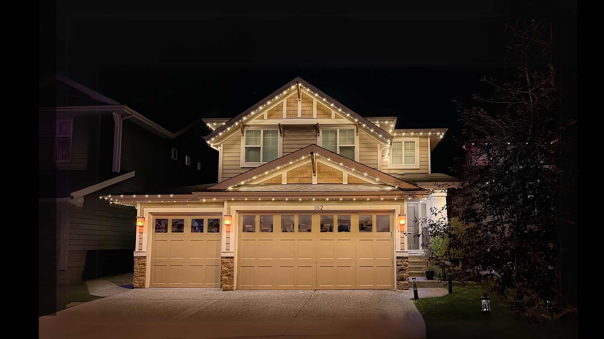 A two-storey home in the evening with warm white roofline lighting and a lit garage front.